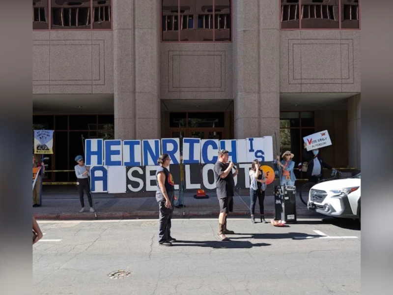 A speaker addresses the crowd in front of a sign reading “Heinrich is a sellout” during a rally outside U.S. Sen. Martin Heinrich’s downtown Albuquerque office Tuesday, Oct. 27, 2026. Students and community members marched from the University of New Mexico to protest AI data centers and the Heinrich-backed Bipartisan American Affordability and Jobs Act. (Kevin Hendricks/The Paper)